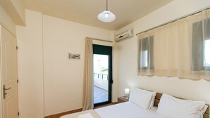 A hotel room with a bed, a nightstand, a window with curtains, an air conditioning unit, and a door leading to a balcony.