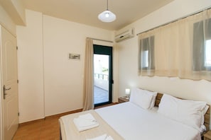 Een hotelkamer met een bed, nachtkastje, raam met gordijnen, airconditioning en een deur naar een balkon.