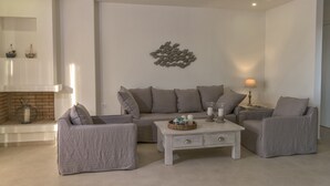 A modern living room with a grey sofa, two armchairs, a white coffee table, and a fireplace. - New Villa Louisa by the sea, walking distance from sea and shops, no car needed! (Πάνορμος)