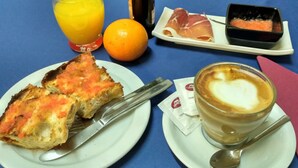 Ein Frühstückstisch mit Toast, Orangensaft, einem heißen Getränk und einer Platte Prosciutto.