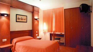 Ein Hotelzimmer mit Bett, Schreibtisch, Stuhl, Lampe, Kleiderschrank und einem gerahmten Bild an der Wand.