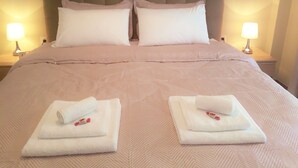 Un lit bien fait, avec deux oreillers et deux serviettes pliées, chacune ornée d’un petit motif rouge.