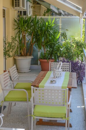 Une terrasse extérieure avec une table en bois, des chaises blanches dotées de coussins verts et diverses plantes en pot.