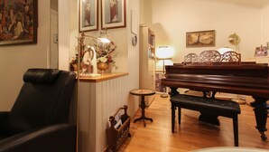 Ein Wohnzimmer mit Klavier, einem schwarzen Ledersessel, einem kleinen runden Tisch und einer dekorativen Vase mit Blumen.