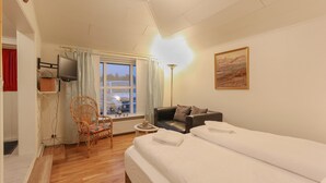 Ein Hotelzimmer mit Bett, Sofa, Sessel, Fernseher, Lampe und einem Fenster mit Blick.