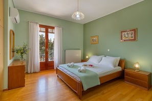 A bedroom with a wooden bed, a nightstand, a bedside lamp, a window with curtains, and a view of the outdoors.