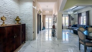 A spacious living area with a marble floor, a dark wooden cabinet, a chandelier, and a modern sofa. - City center apartment with ROOFTOP swimming pool (Χανιά)