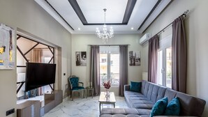 A modern living room with a large flat-screen TV, a sofa, a coffee table, and a chandelier. - City center apartment with ROOFTOP swimming pool (Χανιά)