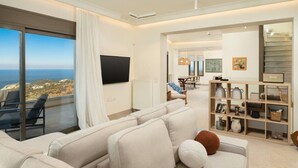 Een moderne woonkamer met een grote bank, een flatscreen televisie en uitzicht op zee.