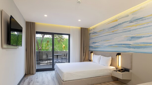 Una camera d'hotel moderna con un letto grande, una TV a parete, un comodino con una lampada e una porta scorrevole in vetro che dà su uno spazio all'aperto.