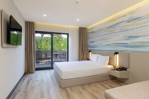 A modern hotel room with a large bed, a TV mounted on the wall, a bedside table with a lamp, and a sliding glass door leading to an outdoor area. - Fora Inn Lara (Antalya)