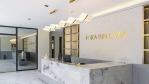Una reception con piano in marmo e divisorio in vetro, una targa appesa al muro con la scritta "FORA INN LARA" e un moderno lampadario sopra la scrivania.