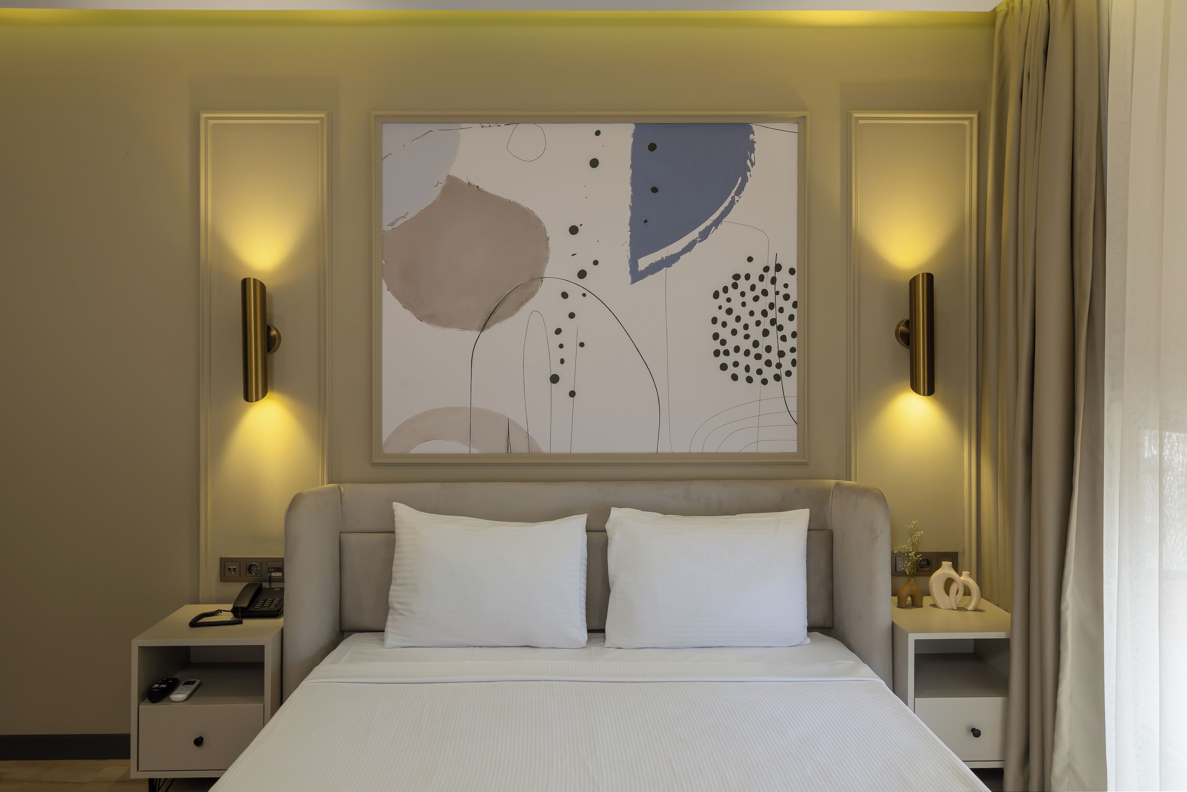 Habitación de hotel con una cama grande, dos mesitas de noche, una obra de arte abstracta en la pared y dos apliques.