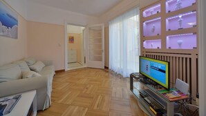 A living room with a sofa, a television, and a shelf with decorative items. - Jasmine in the heart of Kolonaki. (Αθήνα)