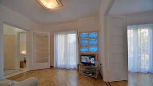 A spacious living room with wooden flooring, a television on a stand, and a door leading to another room. - Jasmine in the heart of Kolonaki. (Αθήνα)