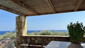 Un mur de pierre donnant sur la mer, un banc en bois, une table et une plante en pot.