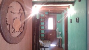 Una puerta de madera con un diseño tallado de elefante, una cama pequeña con una colcha estampada, una escalera de madera y una ventana con una persiana blanca.