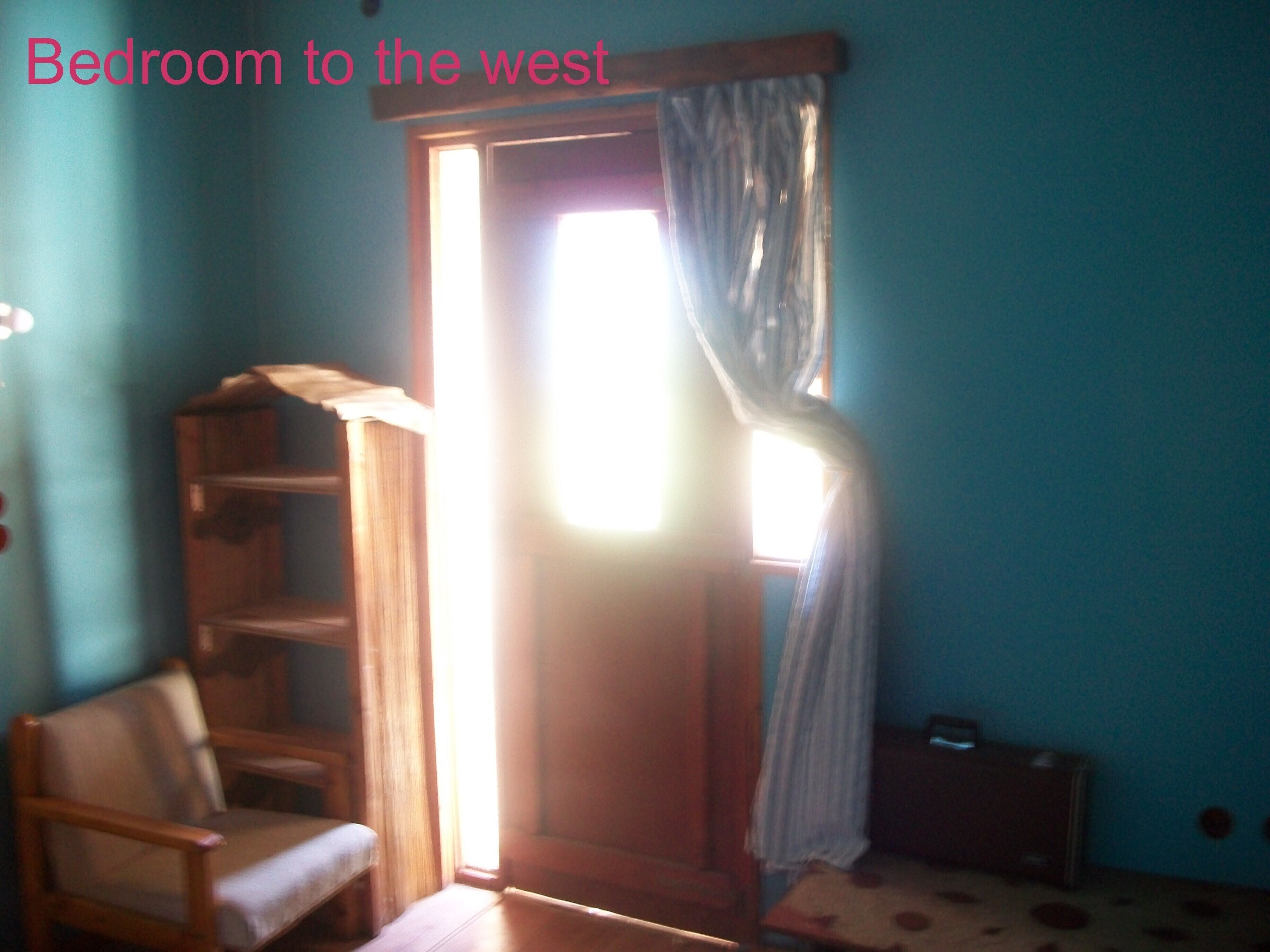 Une chambre à coucher avec une chaise en bois, une petite table et une fenêtre avec des rideaux.