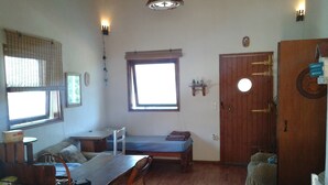 Una habitación pequeña con una mesa de madera, sillas, una cama individual y una puerta de madera.