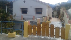Una casa blanca con techo de tejas, cerca de madera y un pequeño jardín con plantas en macetas.