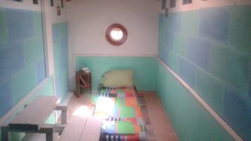 A small, single-bed room with a wooden bench, a small stool, and a colorful quilt on the bed.