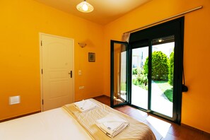 A bedroom with a bed, a door, and a sliding glass door leading to a garden. - Eleanna villas. Villa Athena (Καβρός)