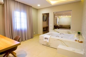 A modern hotel room with a marble bathtub, a wooden dining table, and a large window with curtains. - Hotel Iporã (Itapetininga)