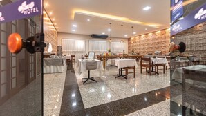 Un restaurante de hotel con varias mesas y sillas, pared de ladrillo e iluminación en el techo.