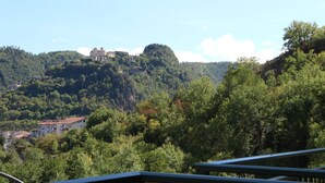 A mountainous landscape with a building on a hill and a house in the foreground. - Palia's Hotel (Laino Borgo)