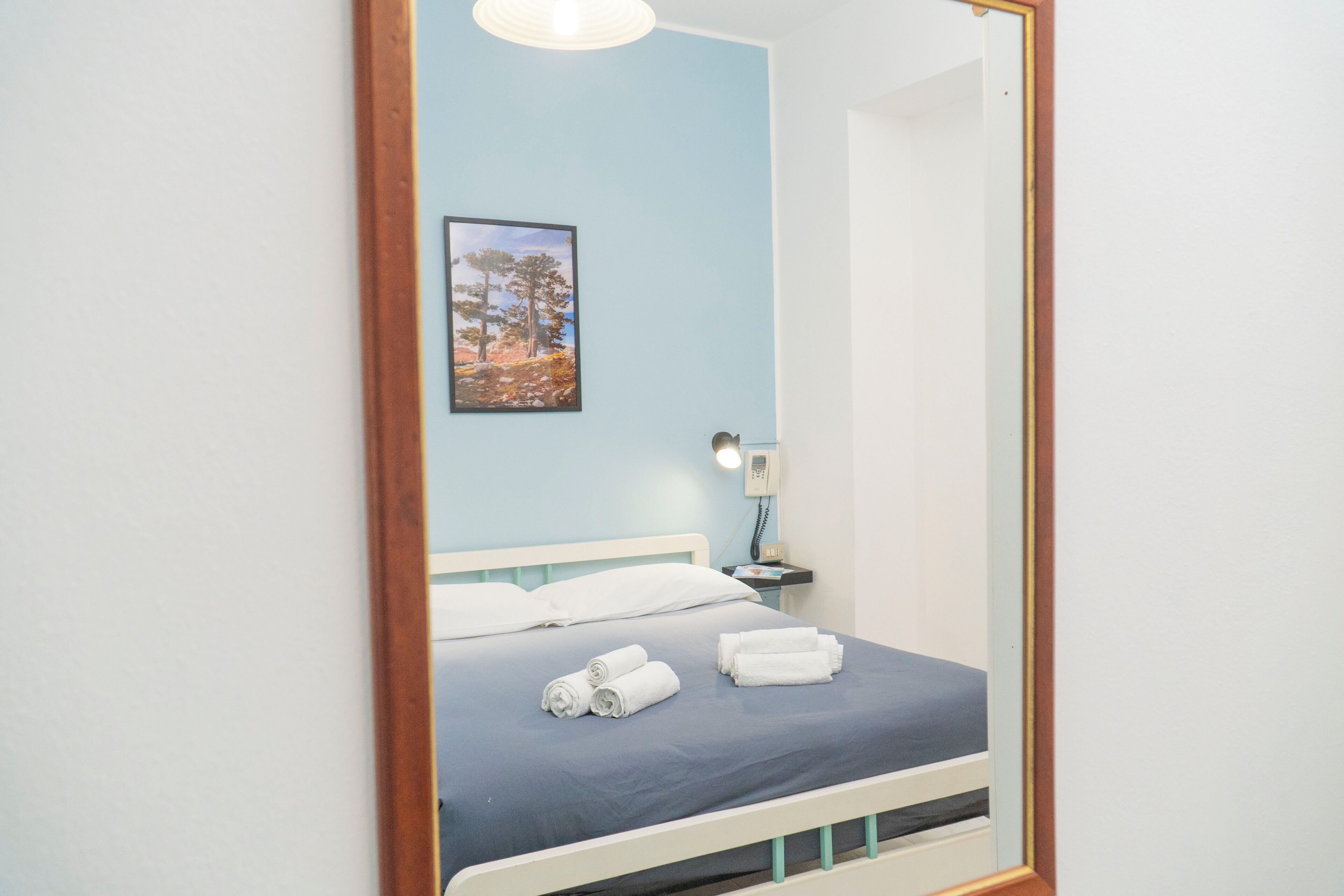 A neatly made bed with white linens and a blue bedspread, a bedside table with a lamp, and a framed picture on the wall.