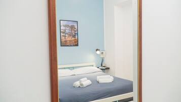 A neatly made bed with white linens and a blue bedspread, a bedside table with a lamp, and a framed picture on the wall.