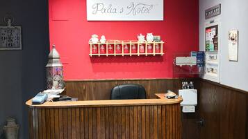 Una recepción con detalles de madera, una pared roja con un letrero que dice "Palia's Hotel" y una estantería con adornos.