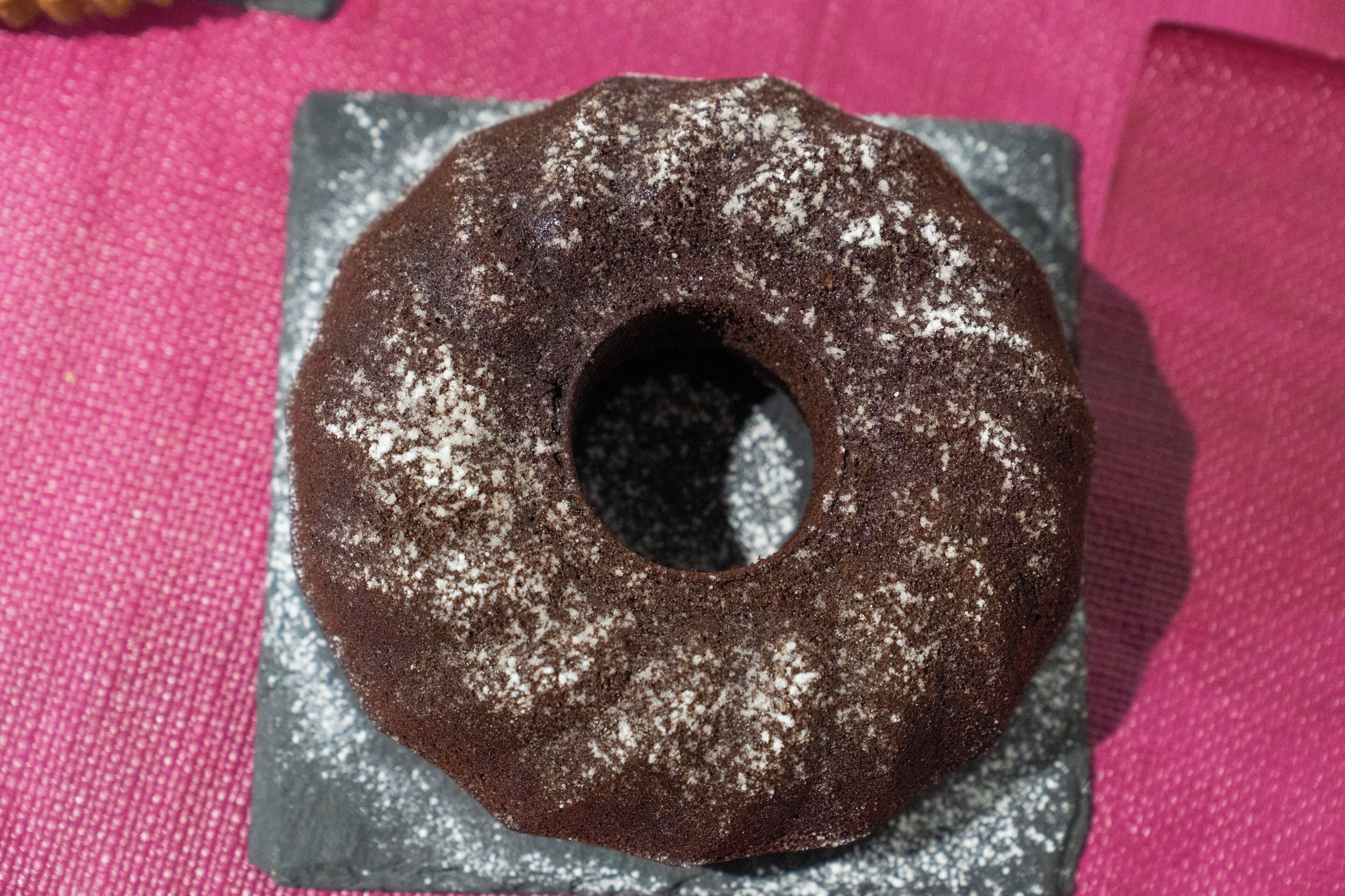 Un pastel de chocolate con azúcar glas sobre un plato oscuro.