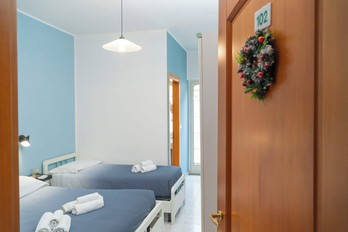 Een hotelkamer met twee bedden, een houten deur met een nummerbord en een lamp.