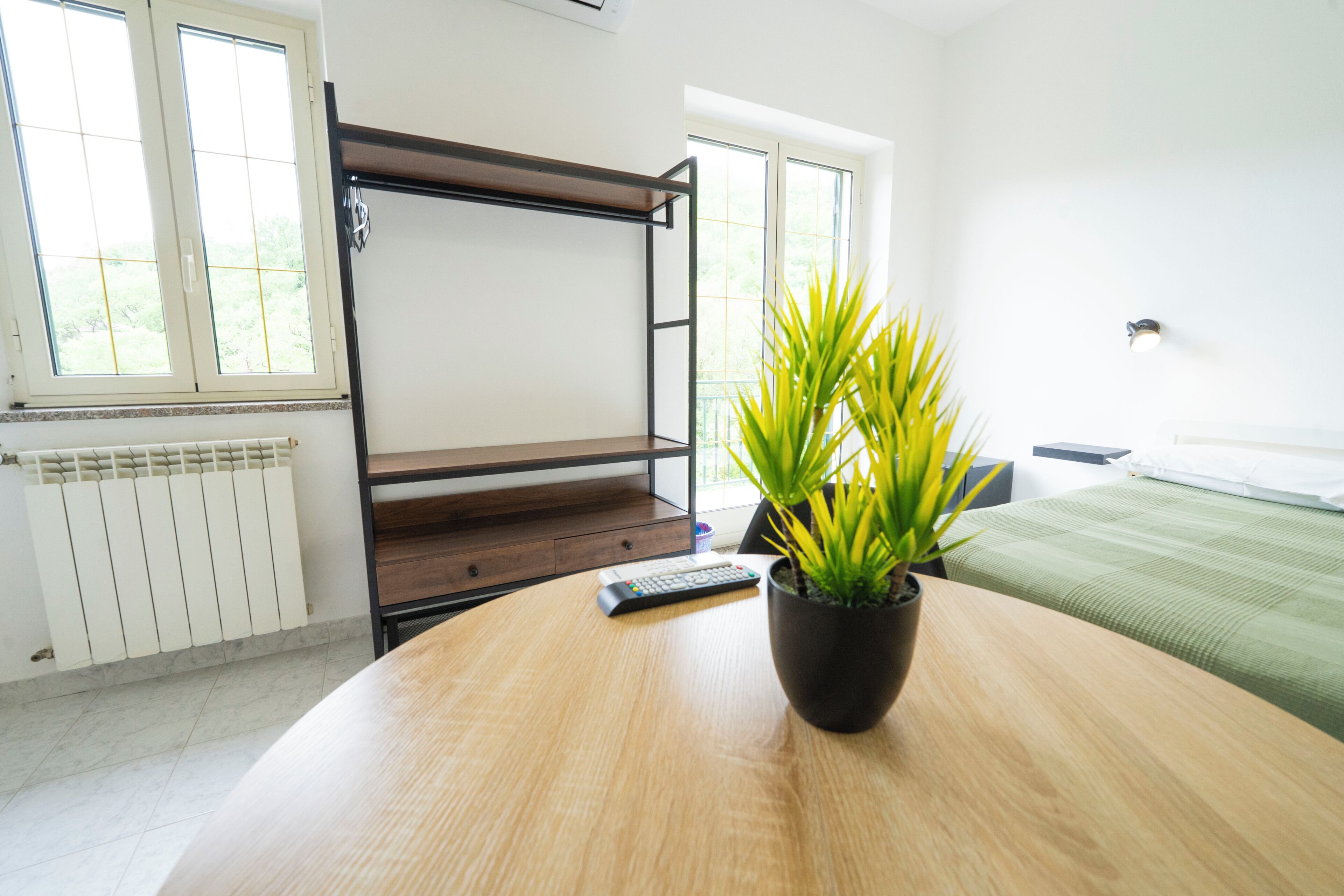 Una habitación con literas, una planta en maceta sobre una mesa de madera, un control remoto y una cama con colcha verde.