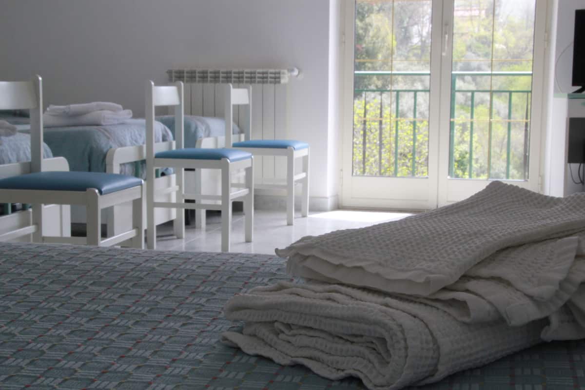 Een slaapkamer met een bed, twee stoelen, een raam met uitzicht op groen en een radiator.