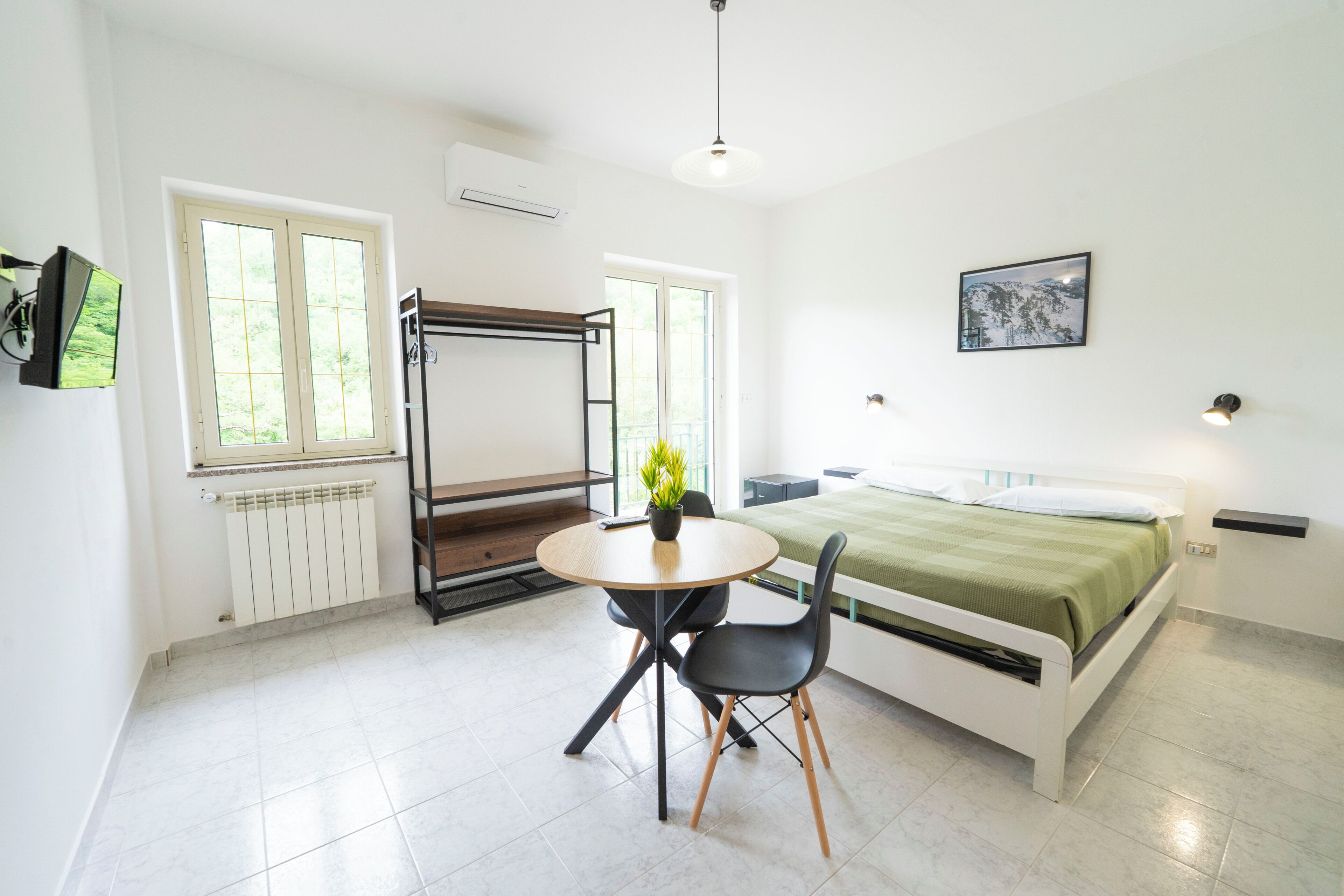 Una habitación con cama, una mesa con sillas, un radiador y una ventana.