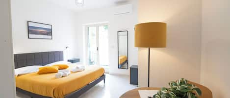 A modern hotel room with a bed, a desk, a lamp, and a plant.