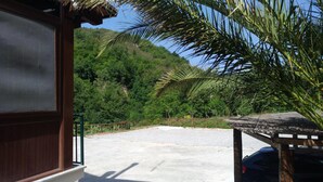 A view from a window overlooking a parking area with a mountain backdrop, a palm tree, and a wooden structure. - Palia's Hotel (Laino Borgo)
