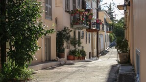 A narrow street lined with buildings featuring balconies with potted plants and flowers. - Under the Clock Tower (Greek Traditional 125m² home) (Ναύπλιο)
