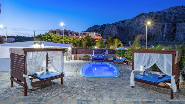 Zona piscina con due aree salotto ombreggiate, un patio in pietra e montagne sullo sfondo.