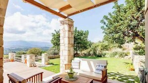An outdoor patio with a wooden table and chairs, a stone pillar, and a view of the countryside.