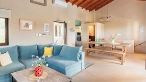 A modern living room with a blue sofa, a wooden coffee table with a flower vase, and a wooden dining table with benches.