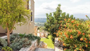 A garden with a view of distant hills, a stone wall, and a building with a window.