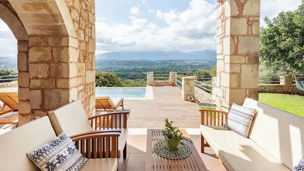 A terrace with stone pillars, wooden furniture, and a view of a mountainous landscape.