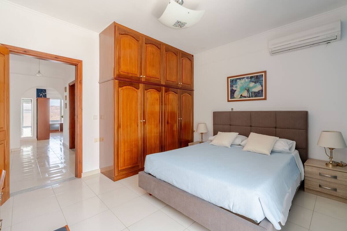 A bedroom with a large bed, wooden wardrobe, and a painting on the wall.
