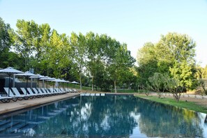 Ein Swimmingpool mit Liegestühlen und Sonnenschirmen, umgeben von Bäumen.