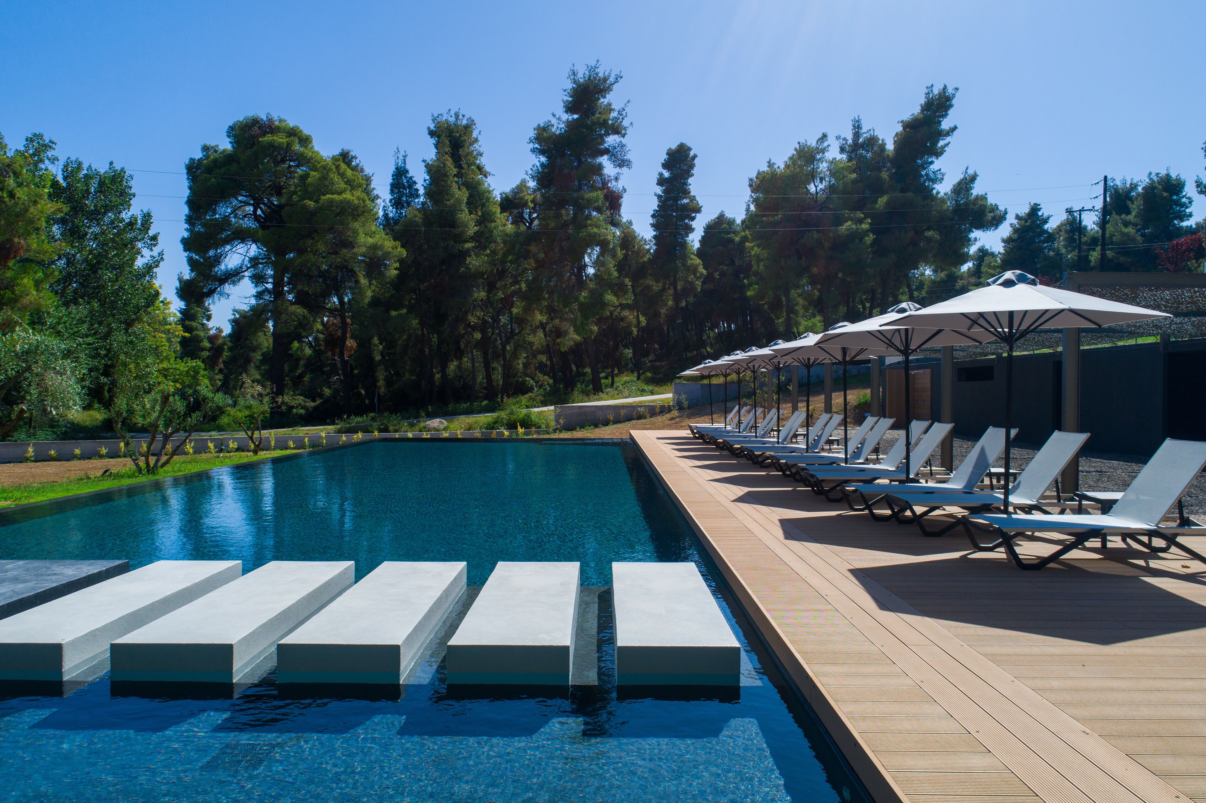 A swimming pool with steps leading into it, surrounded by lounge chairs and umbrellas.