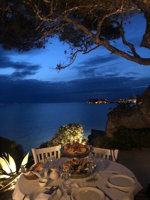 A table set for dinner with seafood and bread, overlooking a coastal view at dusk. - Sani More & Sani Woods (Kassandra)