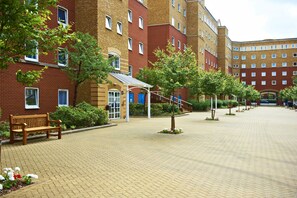 A courtyard with a brick building, a wooden bench, and a covered seating area. - Great Dover Street Apartments (London)